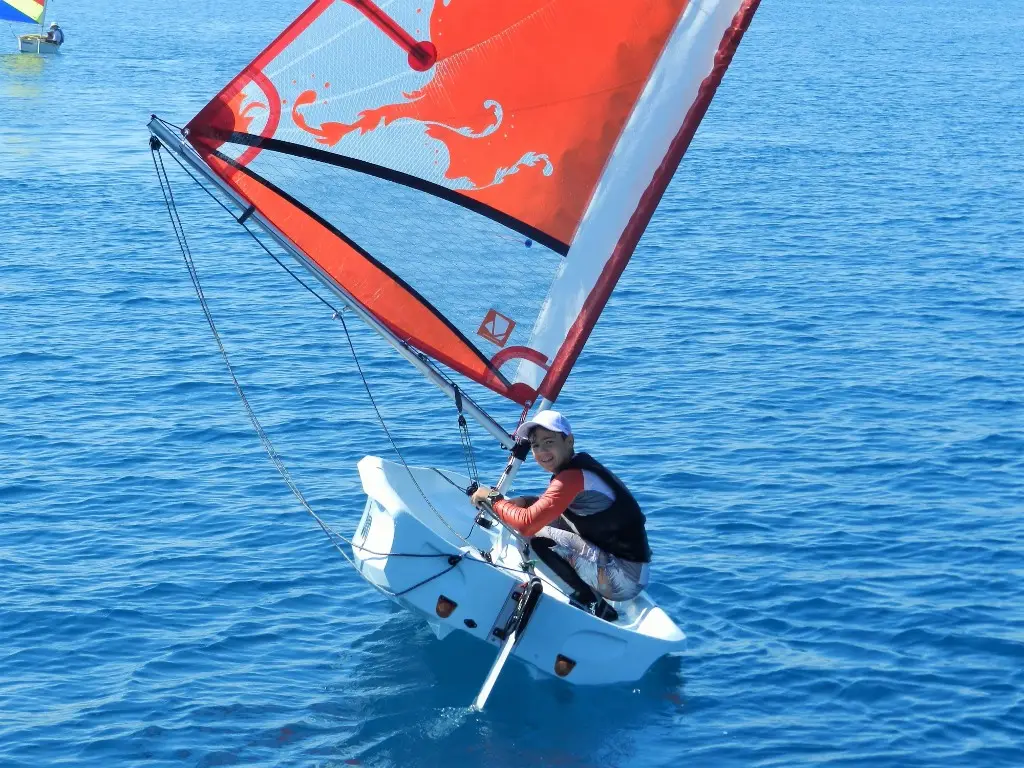 Young sailor in a small dinghy with a red sail